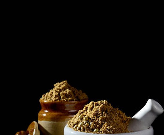 Seeds and Coriander Powder in clay pot and mortar with pestle on black background.